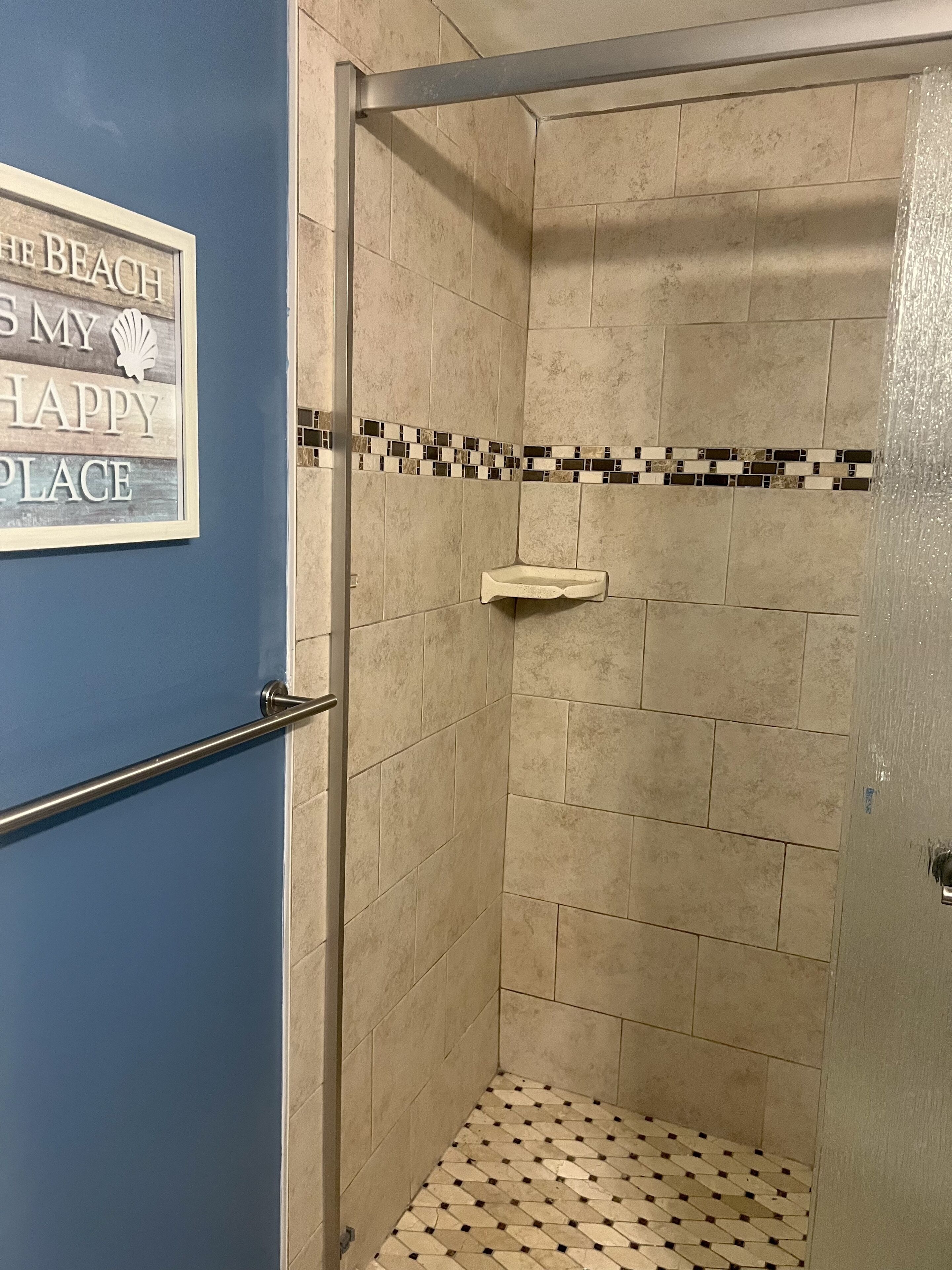 Une douche aux carreaux beiges, un mur bleu et une pancarte sur laquelle on peut lire : « La plage est mon endroit préféré. »