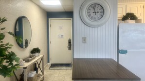 A hallway with a mirror, a clock, a door, and a small table with a plant.