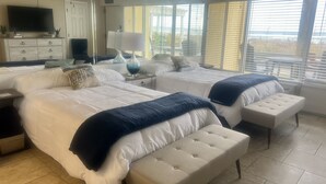A hotel room with two beds, a TV, a desk, and a window with blinds.