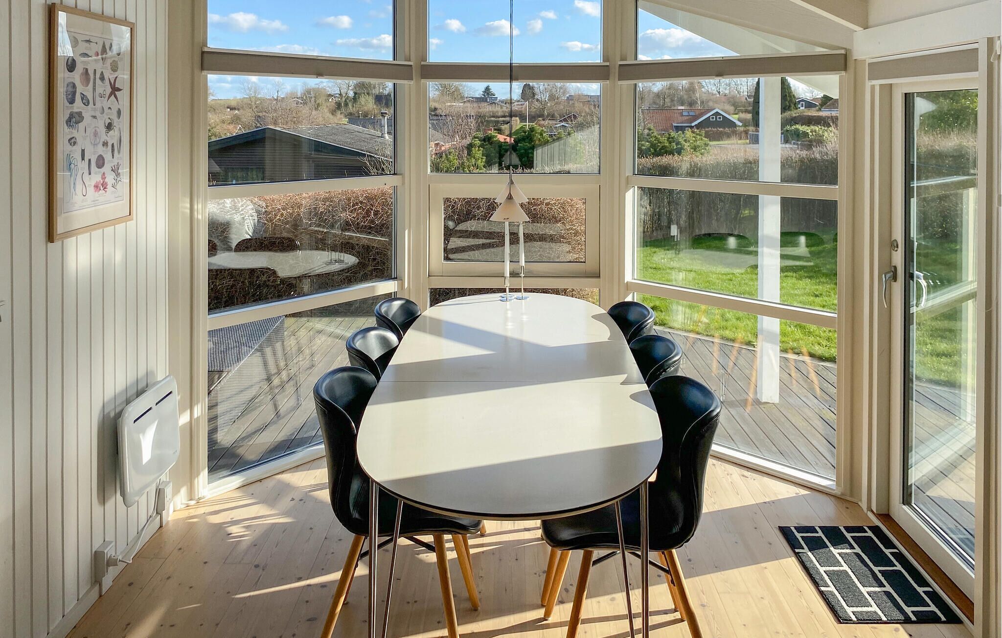 A conservatory with a dining table and chairs, large windows, and a view of the outside.