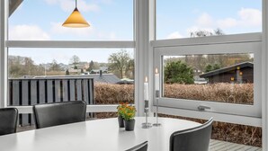 A modern dining area with a white table and chairs, a hanging pendant light, and a view of a residential neighborhood through large windows. - 3 bedroom awesome home in Hejls (Hejls)