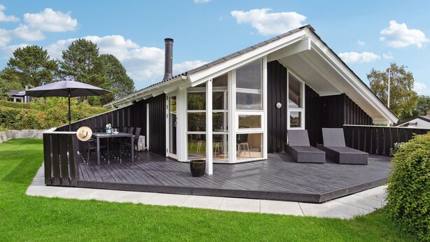 A modern house with a large deck, a dining area, and a lounge with outdoor furniture. - 3 bedroom awesome home in Hejls (Hejls)