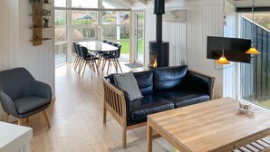 A modern living room with a black leather sofa, a wooden coffee table, a dining table with chairs, and a fireplace. - 3 bedroom awesome home in Hejls (Hejls)