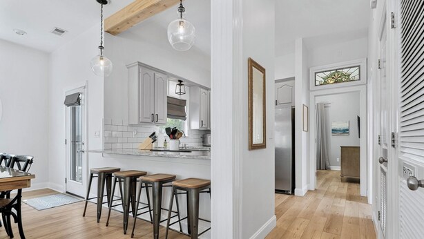 A modern kitchen with white cabinets, a wooden dining table, and bar stools. - Private Heated Pool - 3 Min Walk to Beach - Golf Cart - Beach Chair Service (Destin)