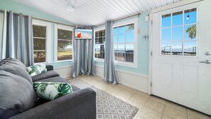 A room with a grey sofa, a patterned rug, a television, and a door with a view of the outside.