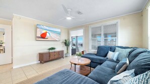 A living room with a sectional sofa, a round coffee table, a TV mounted on the wall, and a ceiling fan.
