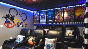 A home theater room with black leather recliners, a wall decorated with movie posters, and a Disney-themed wall decal. - Lakeview 9BR | Spider-Man Game Room, Pool & Spa (Kissimmee)