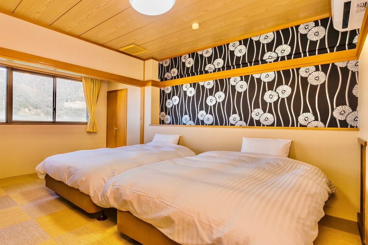 A hotel room with two beds, a window with curtains, a radiator, and a patterned wall.