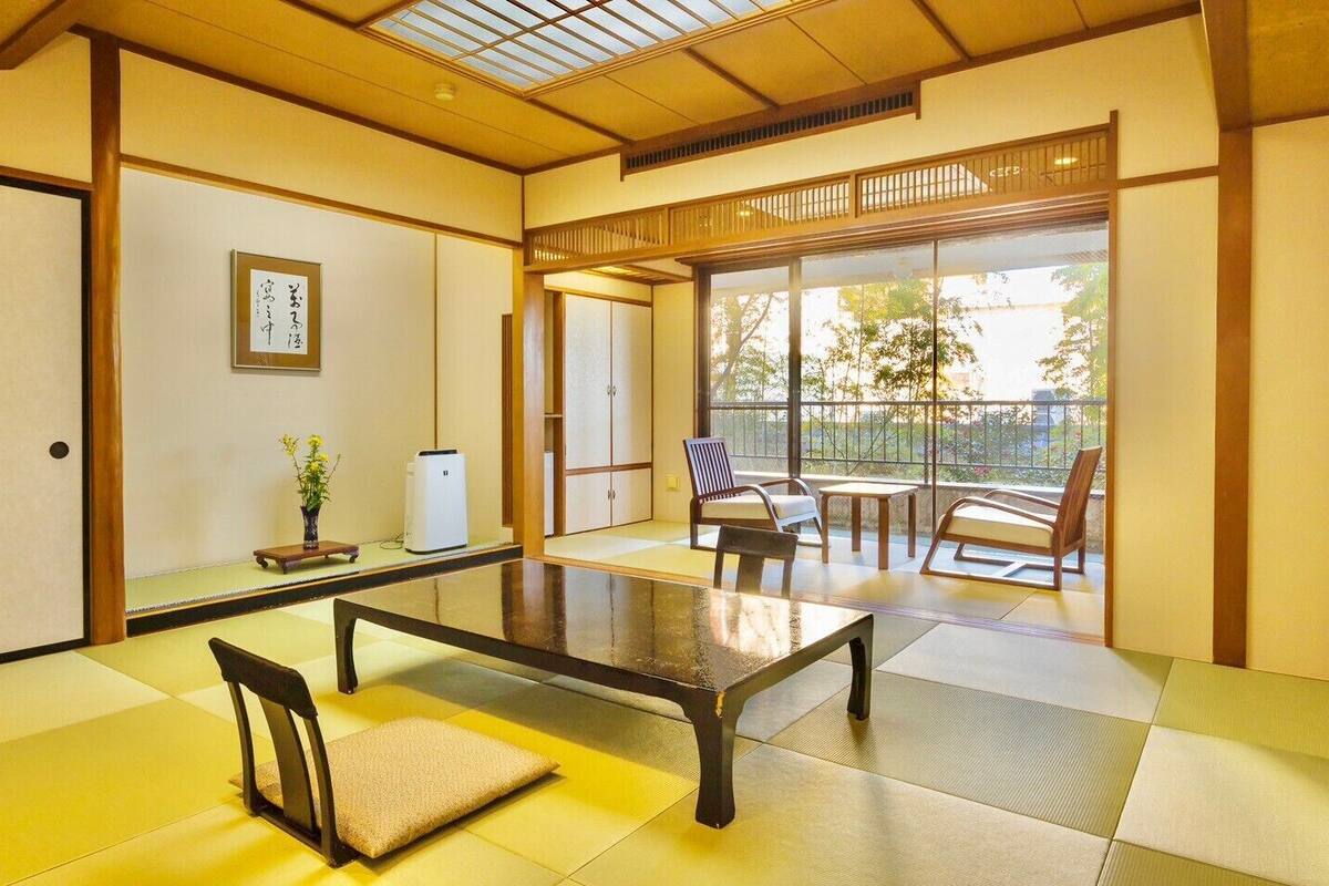 A tatami mat room with a low table, chairs, a heater, and a sliding door leading to an outdoor area.