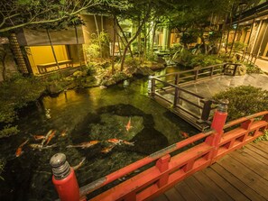 A koi pond with a wooden bridge, surrounded by lush greenery and traditional architecture. - Japanese Onsen Ryokan KOHAKUEN (Fuefuki)
