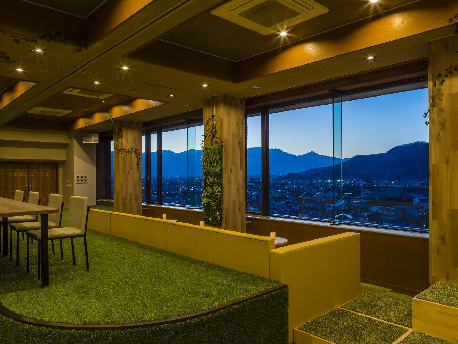 Habitación de hotel moderna con un ventanal grande que ofrece vistas a la ciudad, una zona de estar con césped artificial y detalles de madera.