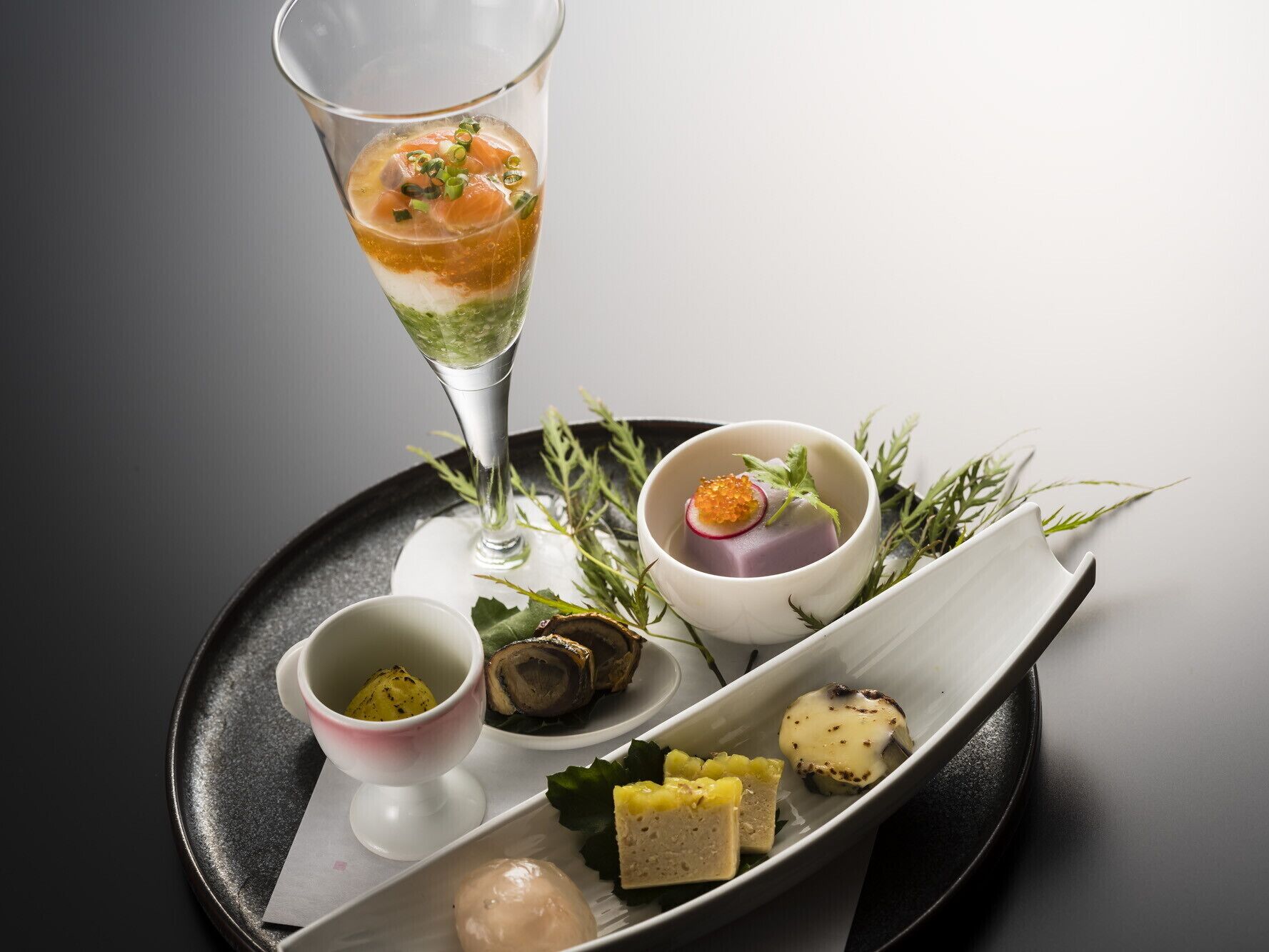 A tray with various food items including a glass of layered drink, a bowl with a purple item and radish, and several small dishes with different food items.