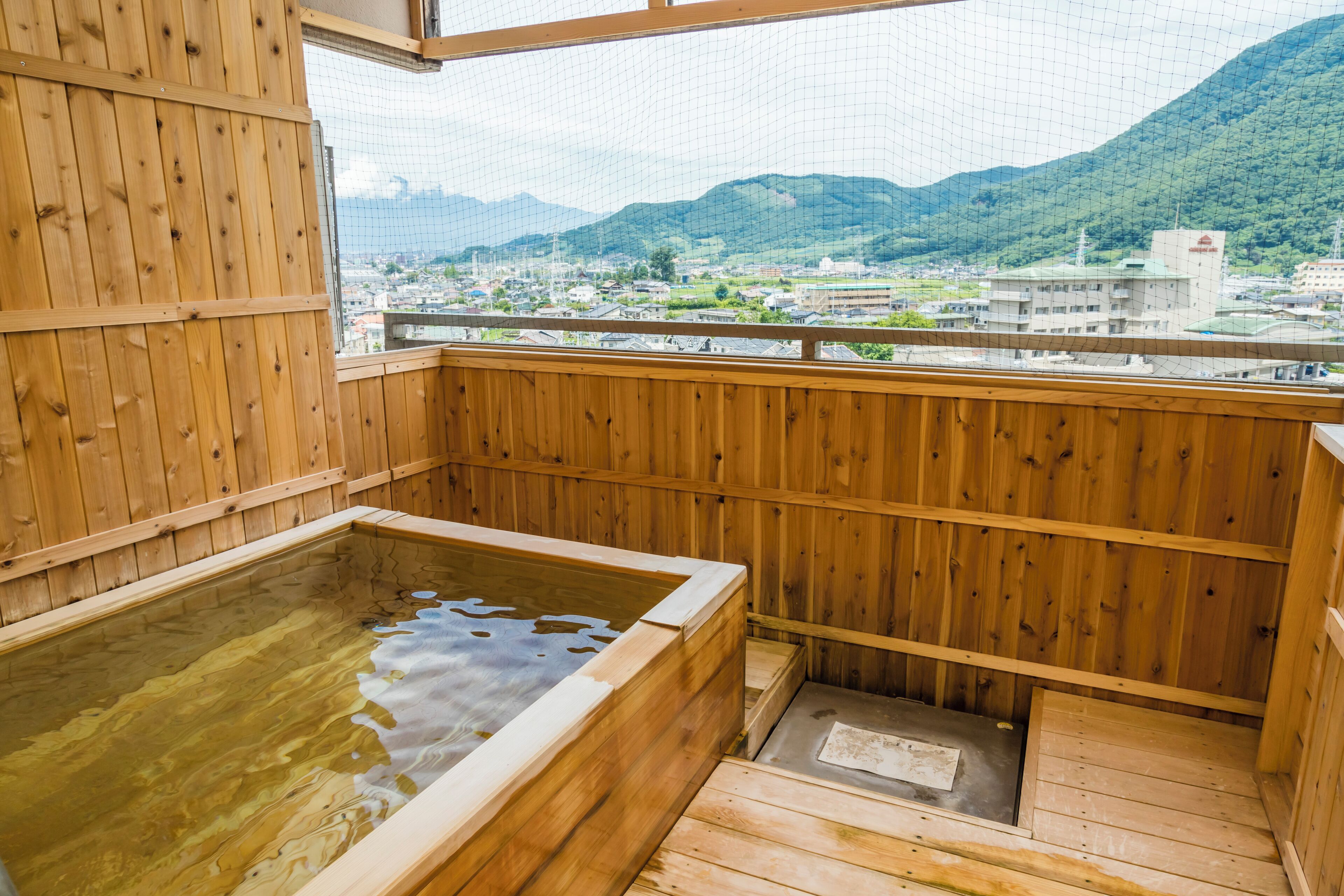 A wooden hot spring bath with a view of a town and mountains.