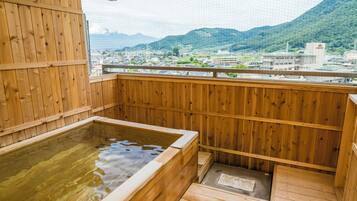 A wooden hot spring bath with a view of a town and mountains.