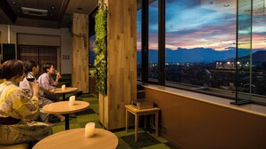 Ein modernes Interieur mit Holzakzenten, runden Tischen und Blick auf eine Stadtlandschaft im Abendlicht.