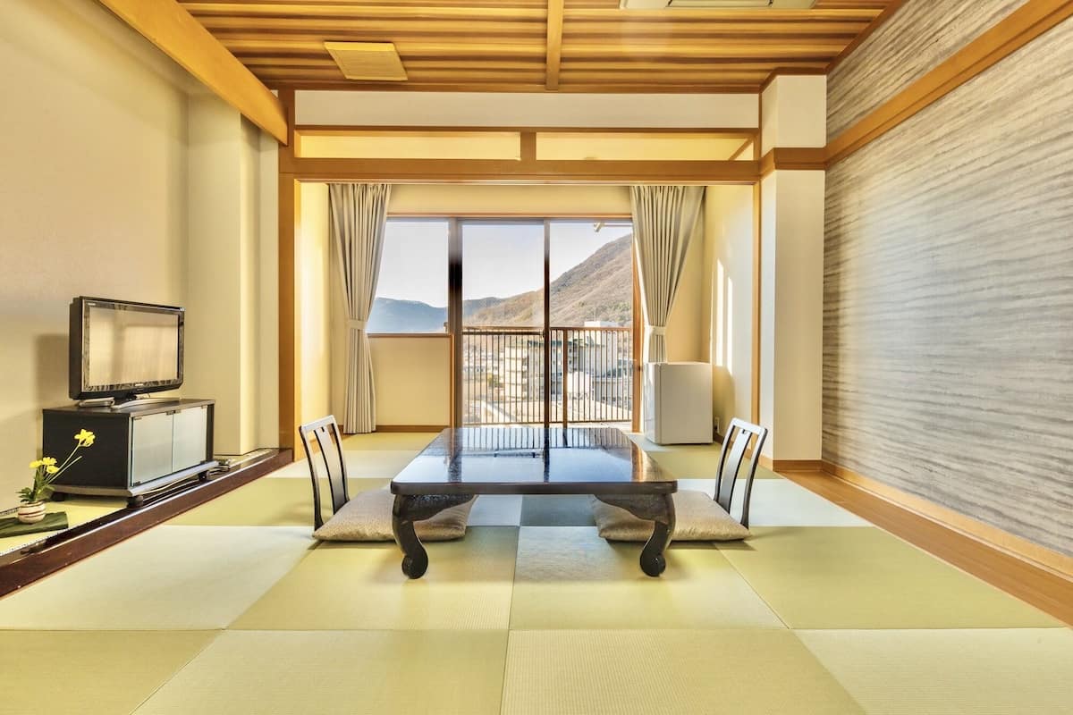 A traditional Japanese room with tatami flooring, a low table, and a television on a cabinet.
