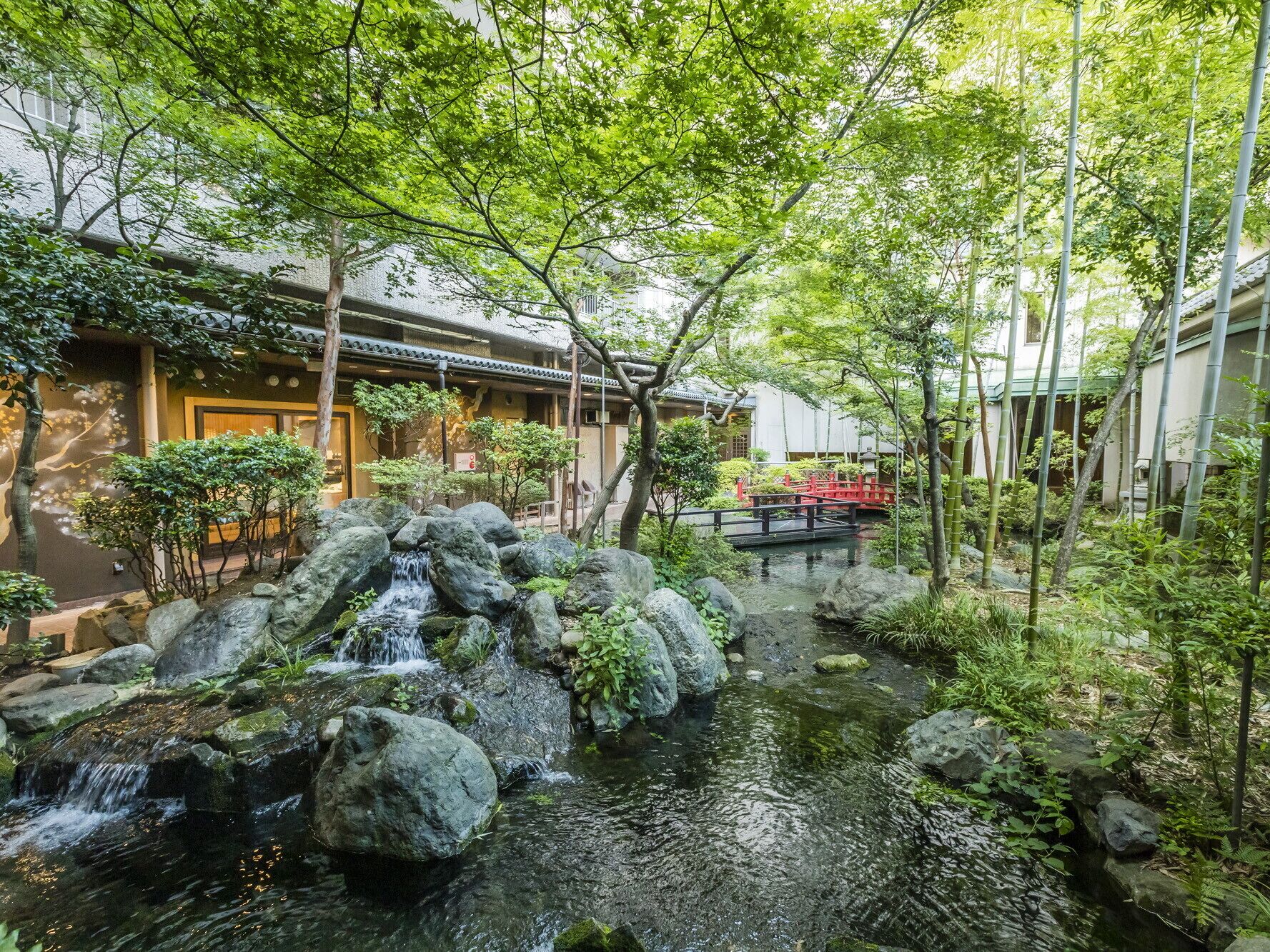 Un jardin japonais traditionnel avec un bassin à carpes koï, des bambous et un pont rouge.