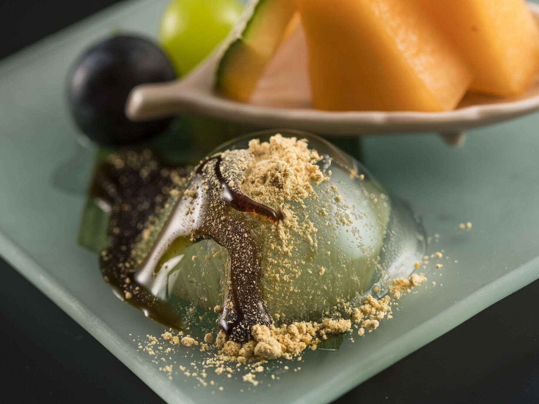 Un dessert servi à la cuillère, un melon et un objet sphérique noir sur une assiette.
