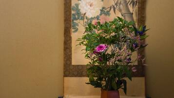 A potted plant with flowers in a room with a patterned wall and a painting.