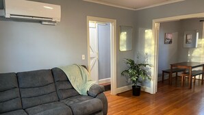A living room with a grey sofa, a potted plant, wooden flooring, and a dining area with a table and chairs. - Hidden Oasis of West Columbia (West Columbia)