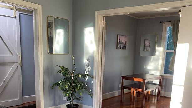 A spacious room with hardwood flooring, a potted plant, a dining table with chairs, and a door leading to another room. - Hidden Oasis of West Columbia (West Columbia)