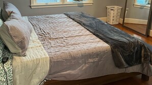 A bedroom with a bed, a ceiling fan, a window with curtains, a mirror, and a laundry basket. - Hidden Oasis of West Columbia (West Columbia)