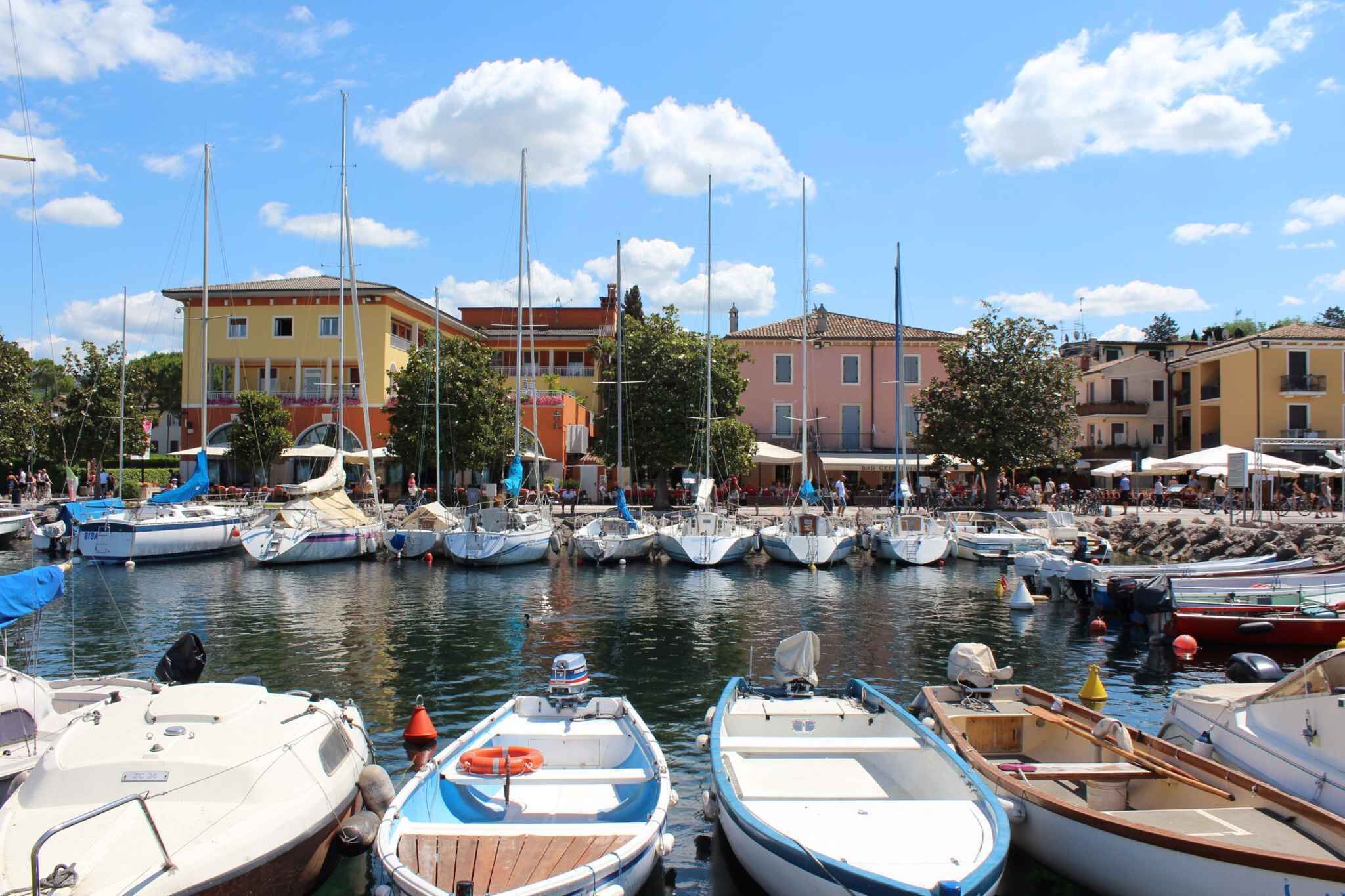 A marina with boats docked, a building with a yellow facade, and a clear blue sky.