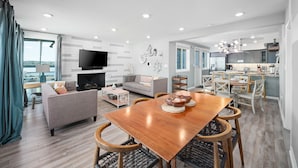 A modern living room with a wooden dining table, grey sofas, and a flat-screen TV. - Bayfront | Ultimate Family Fun | AC | Parking (San Diego)