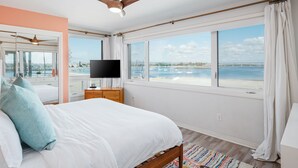 A bedroom with a large bed, a ceiling fan, a TV, and a view of the beach. - Bayfront | Ultimate Family Fun | AC | Parking (San Diego)