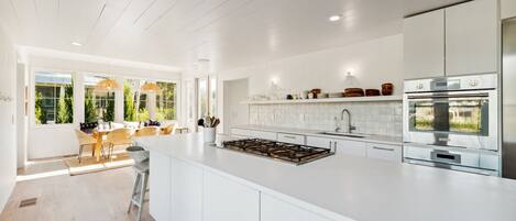 A modern kitchen with white cabinetry, a large island, stainless steel appliances, and a dining area with wicker chairs.