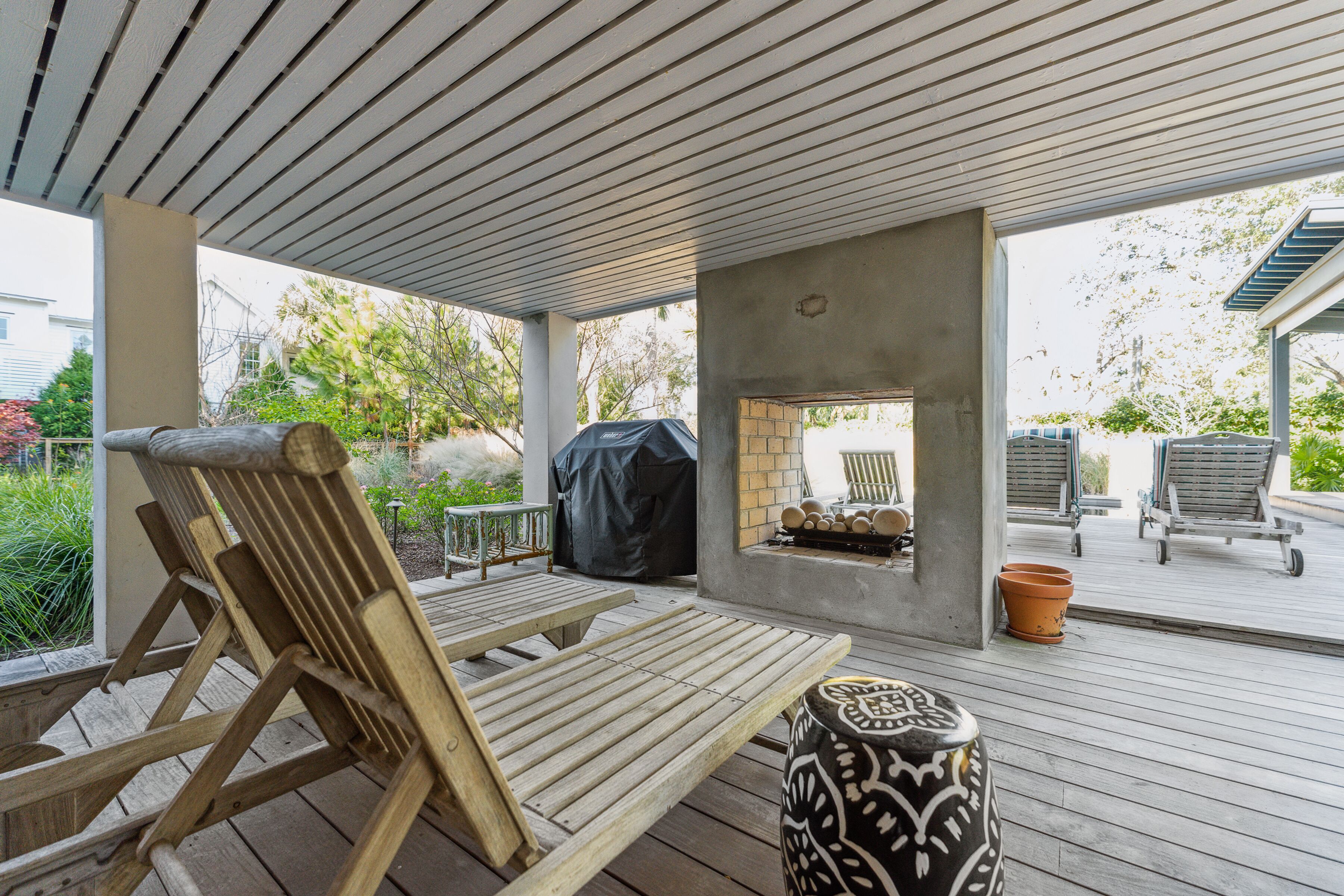 An outdoor patio area with wooden lounge chairs, a barbecue grill, and a decorative urn.