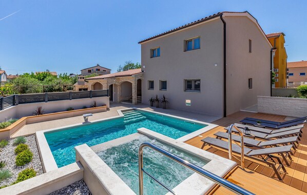 A swimming pool with a sun deck and lounge chairs, surrounded by a building with multiple windows and a stone archway. - Awesome home in Medulin with sauna (Medulin)