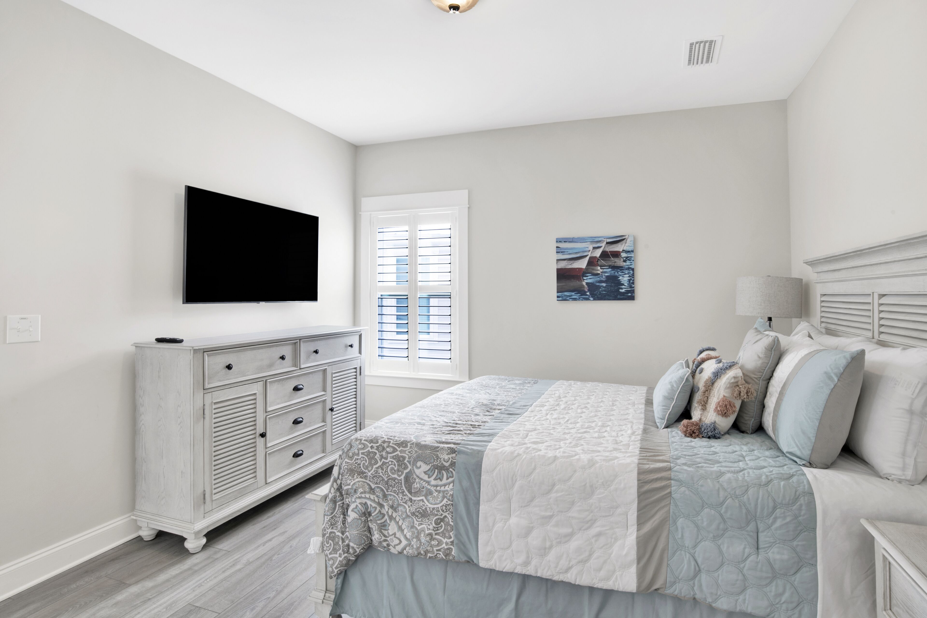 Ein Schlafzimmer mit Bett, Kommode, Fernseher, Fenster und Kunstwerken.