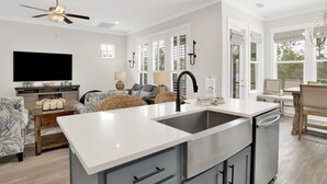 A modern kitchen with a central island, built-in appliances, and a dining area with a chandelier. - 3BR Home @ Summer Salt • Sleeps 13 • Porches, Pool & Near Beach (Orange Beach)