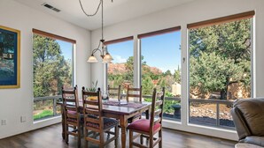 A dining area with a wooden table and chairs, large windows with a view of trees and mountains, and a hanging light fixture. - Stylish and comfortable home in a prime location. Close to golf, hiking & biking (Sedona)