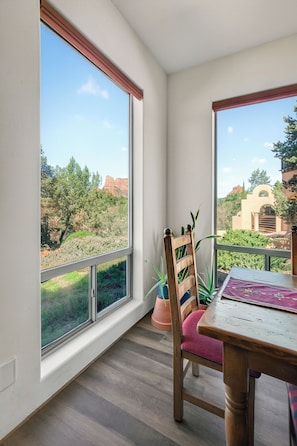Ein Zimmer mit großen Fenstern, einem Holztisch, einem Stuhl und einem Blumentopf.