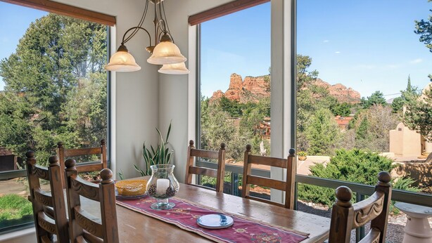 A dining table with chairs, a chandelier, and a view of red rock formations. - Stylish and comfortable home in a prime location. Close to golf, hiking & biking (Sedona)