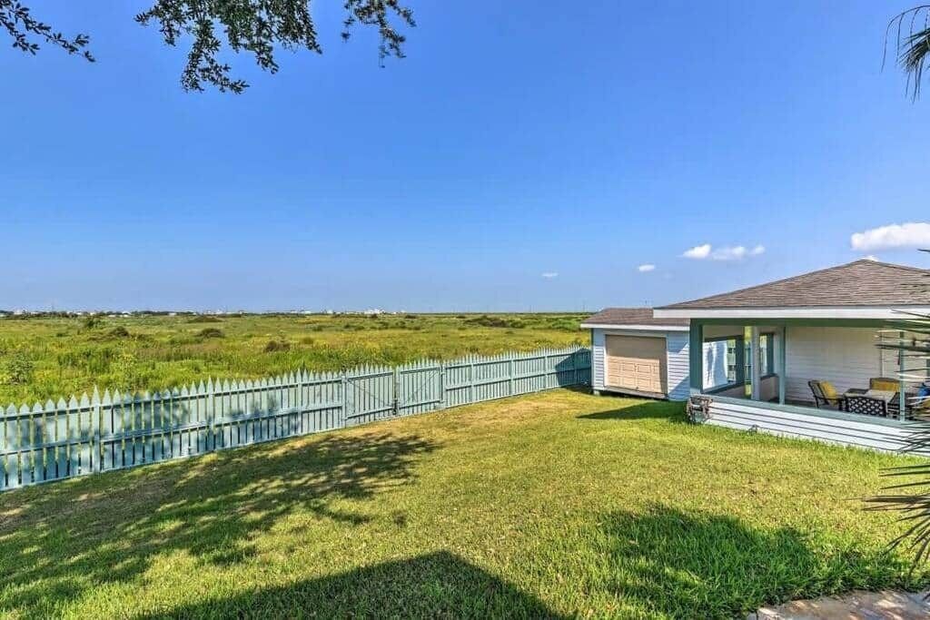 Een huis met een overdekte veranda, een omheind gazon en uitzicht op het omliggende landschap.