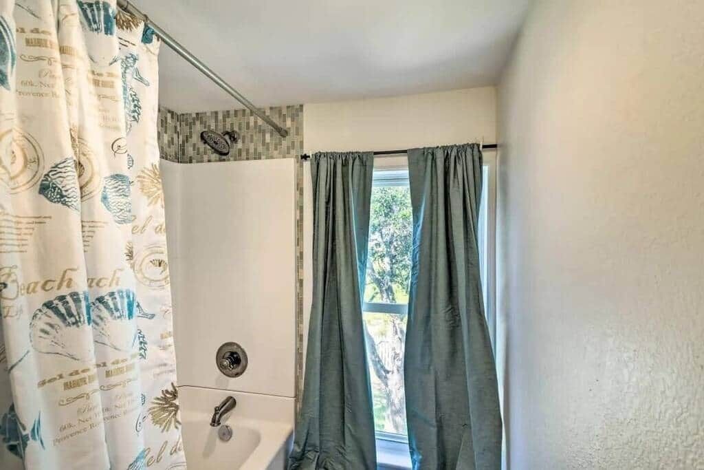 Une salle de bain avec un rideau de douche orné de motifs représentant des créatures marines, une baignoire et une fenêtre avec des rideaux.