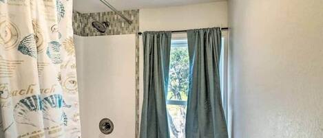 Une salle de bain avec un rideau de douche orné de motifs représentant des créatures marines, une baignoire et une fenêtre avec des rideaux.
