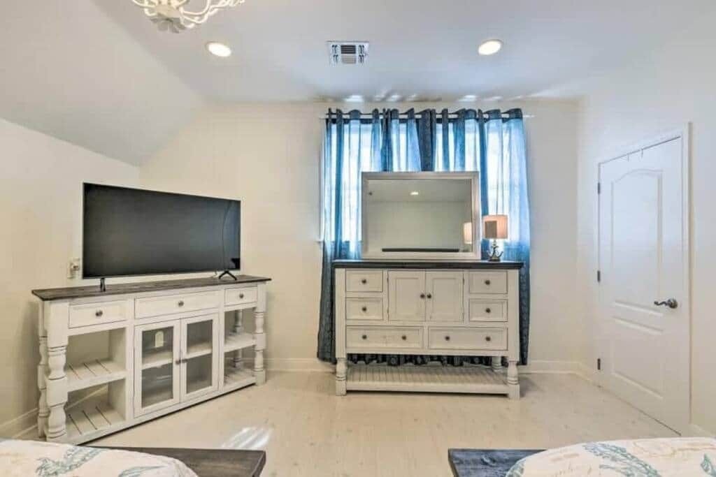 A room with a television on a white cabinet, a mirror above it, and a door to the right.