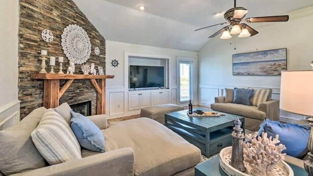 A living room with a stone accent wall, a ceiling fan, a fireplace, and a television. - Absolute Paradise Galveston (Galveston)
