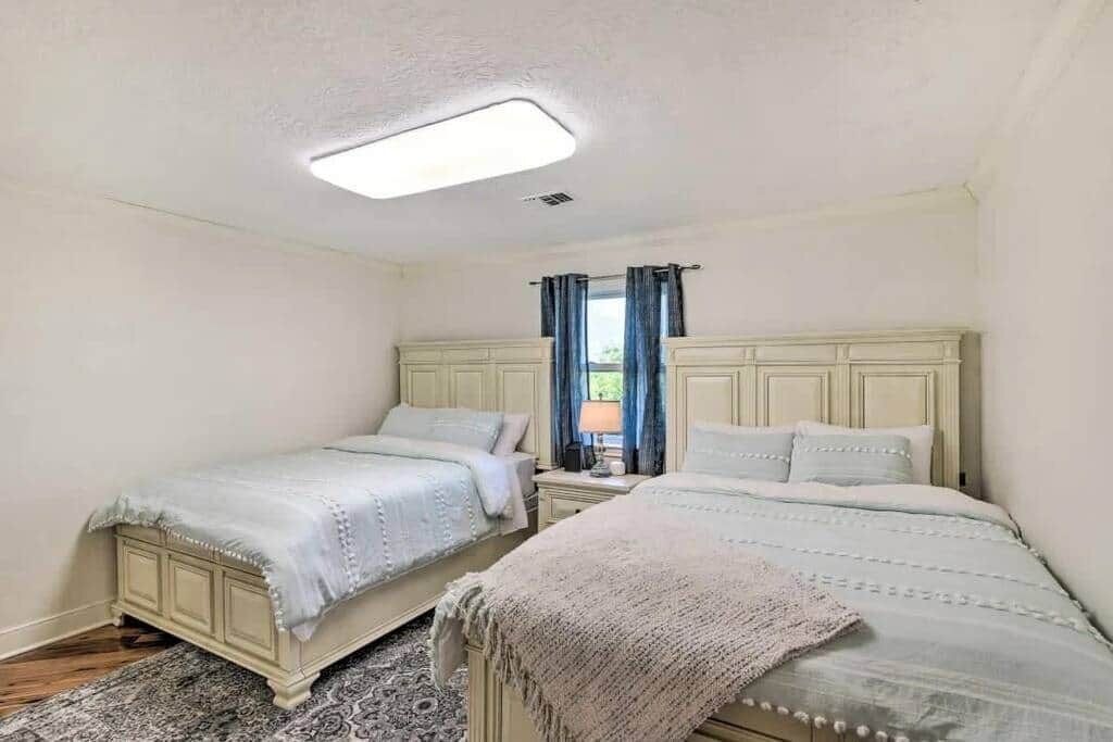 Een slaapkamer met twee bedden, een nachtkastje, een lamp en een raam met gordijnen.