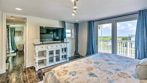 A bedroom with a large bed, a TV, a dresser, and a balcony with a view. - Absolute Paradise Galveston (Galveston)