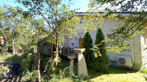 A stone building with a garden area featuring a stone sculpture, a wooden fence, and a stone wall.
