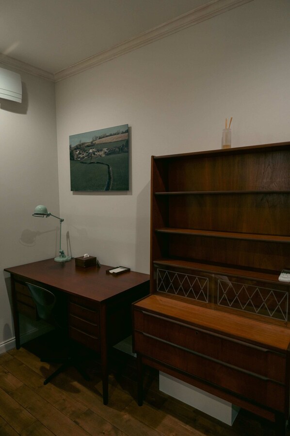 Een kamer met een houten bureau, een stoel, een boekenkast en een schilderij aan de muur.