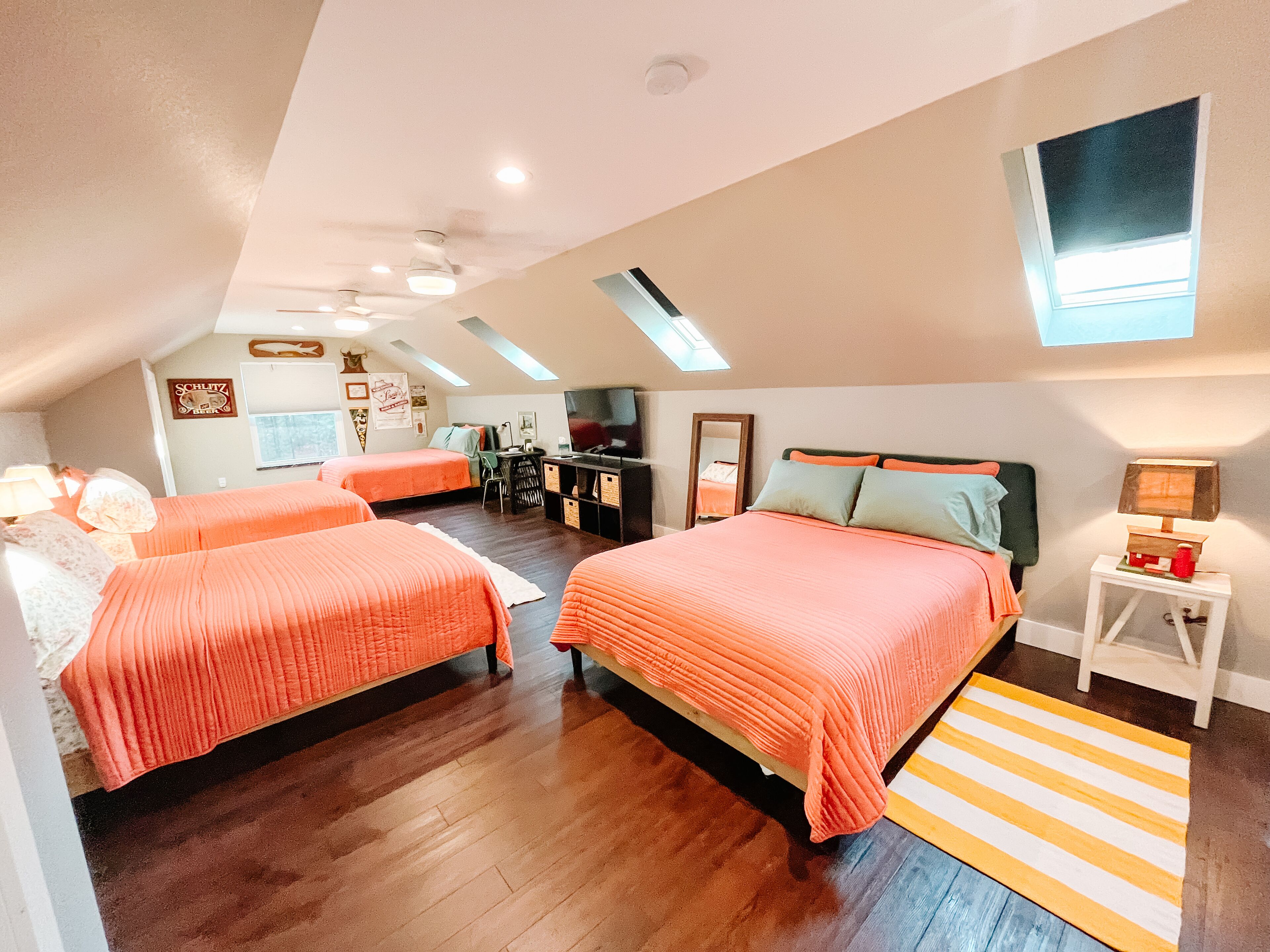 A bedroom with two beds, a desk, a TV, and a skylight.