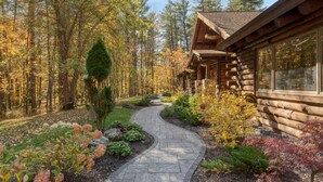 A log cabin with a stone pathway leading to the entrance, surrounded by autumn foliage and a forest backdrop. - Moose Lodge by Avantstay Luxe Berkshires Escape (Great Barrington)