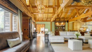 A spacious living area with a wooden ceiling, a sofa, a coffee table, and a dining area in the background. - Moose Lodge by Avantstay Luxe Berkshires Escape (Great Barrington)