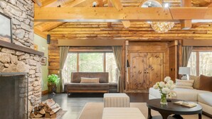 A cozy living room with a stone fireplace, wooden beams, a sofa, and a coffee table. - Moose Lodge by Avantstay Luxe Berkshires Escape (Great Barrington)